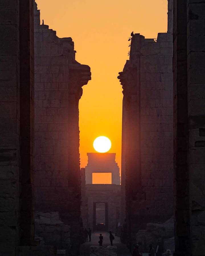 Perfectly aligned sunrise seen through the massive stone doorway of an ancient Egyptian temple.
