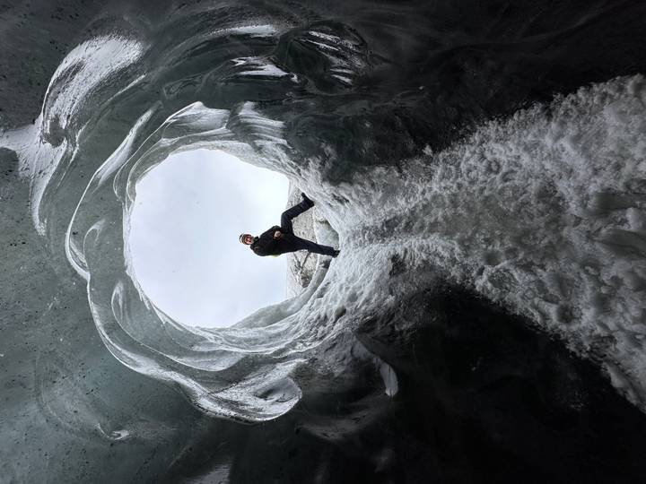 Adventurer poses inside a circular ice cave entrance framed by sculpted blue ice walls