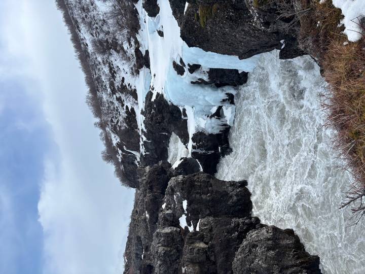 Raging winter waterfall crashes through dark basalt cliffs draped with gleaming blue ice