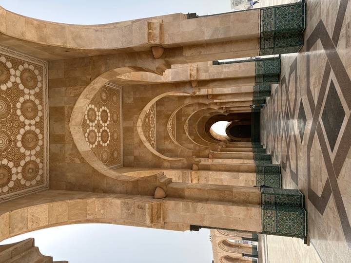 Grand marble arcade of Hassan II Mosque with geometric floor and distant visitors.