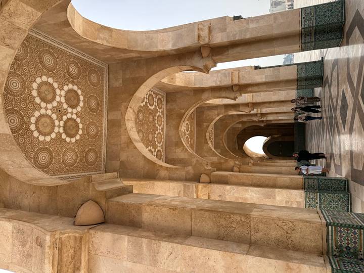 Visitors walk beneath Islamic arches adorned with floral motifs inside a vast mosque corridor.