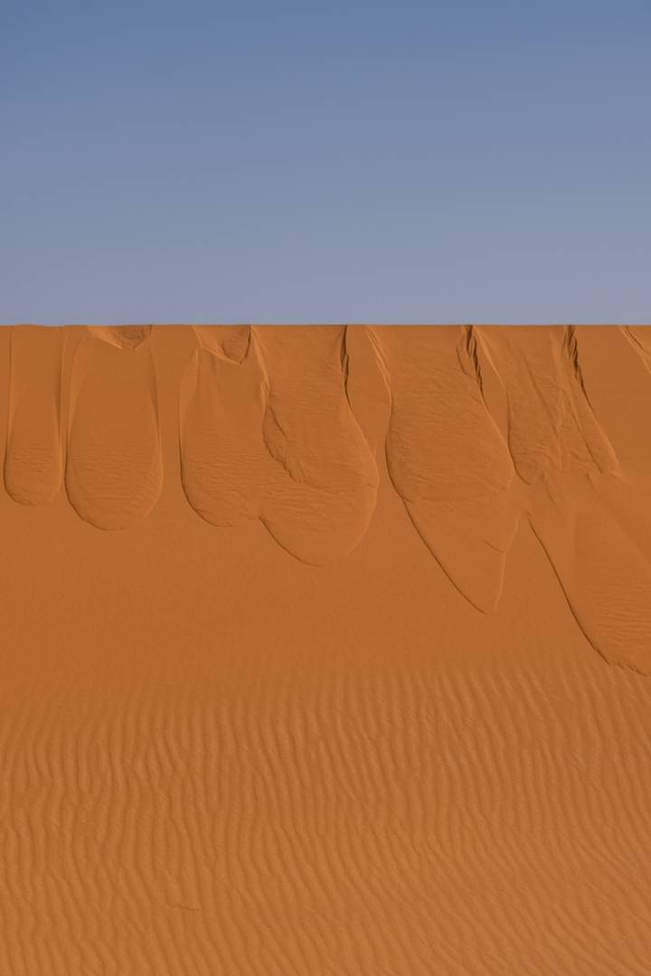 Aerial view of smooth orange sand dunes with elegant wind-carved ridges in the desert.