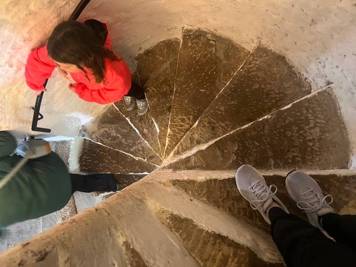 Narrow spiral stone staircase viewed from above with travelers descending.
