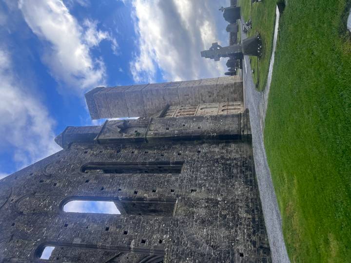 Weathered stone ruins and tall tower of Rock of Cashel framed by vibrant grass and moody clouds.