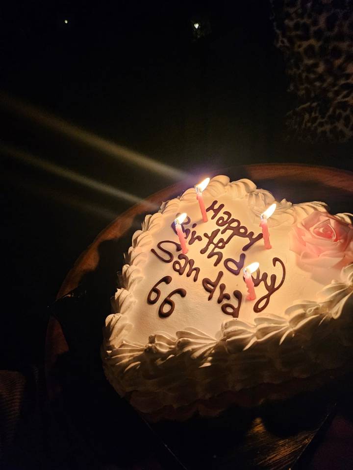 Close-up of frosted birthday cake with lit candles spelling 'Happy Birthday San dia 66'.