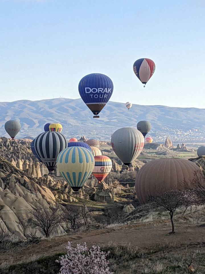 Close-up view of colorful hot-air balloons floating above Cappadocia’s rock formations with distant mountains.