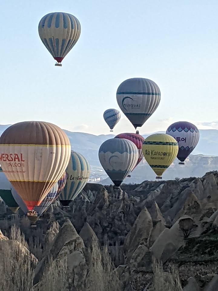 Zoomed-in shot of several hot-air balloons floating above rugged rocky cliffs in Cappadocia.