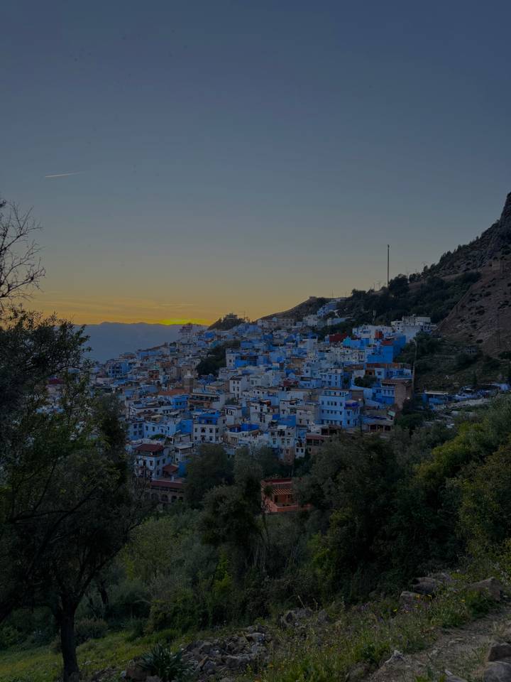 Panoramic dusk view of the blue-painted hillside town with the sun setting behind mountain peaks.