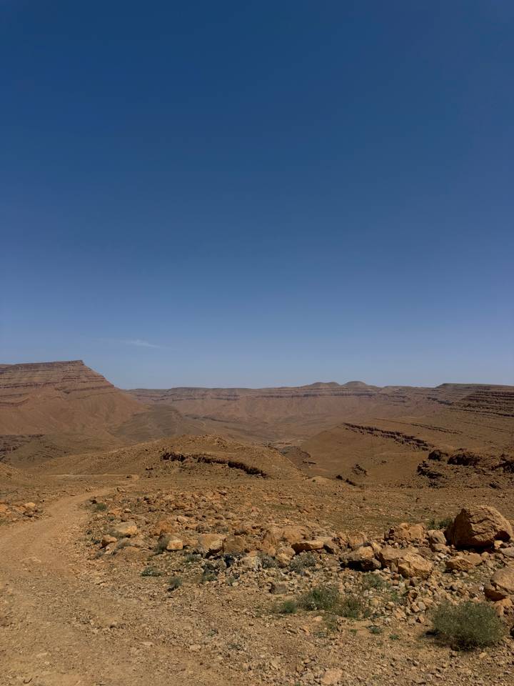 Wide open arid mountain range and barren brown ridges beneath a cloudless blue sky.