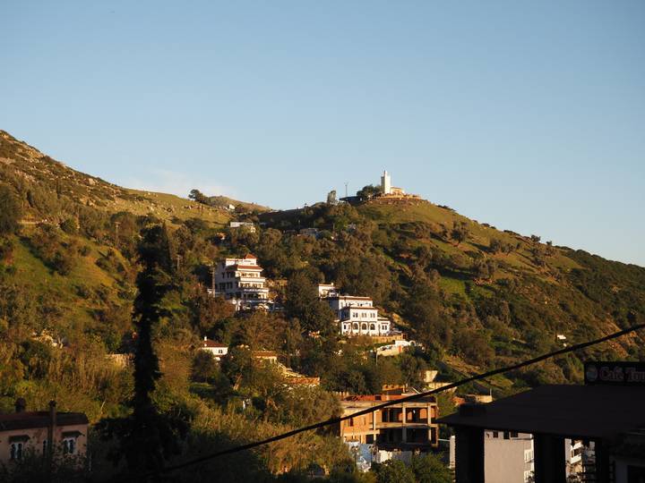 Hillside dotted with white buildings and a small summit shrine under late afternoon light.
