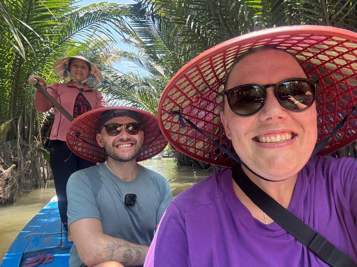 Selfie of two travelers in conical hats on a small rowing boat through palm-lined canal