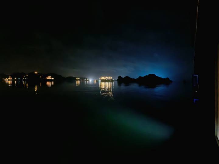 Moody night view of Halong Bay with faintly lit cruise ships reflecting on calm water