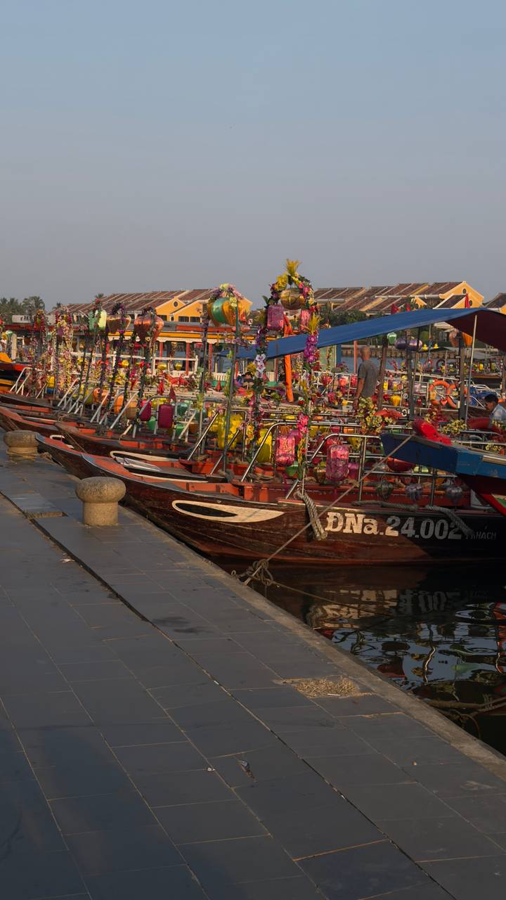 Row of wooden tour boats festooned with colorful lanterns moored along a riverside at sunset