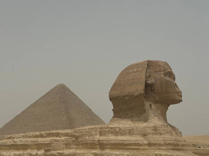 Iconic profile of the Great Sphinx aligned with a pyramid rising in the hazy desert sky.