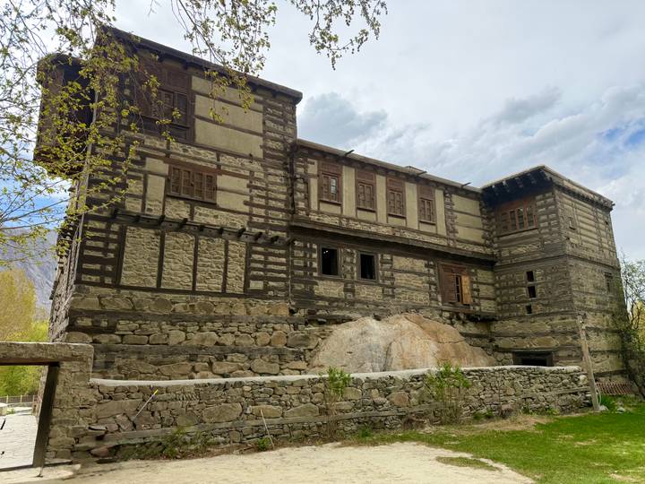 Historic stone and timber fort with small windows set against a cloudy mountain sky.