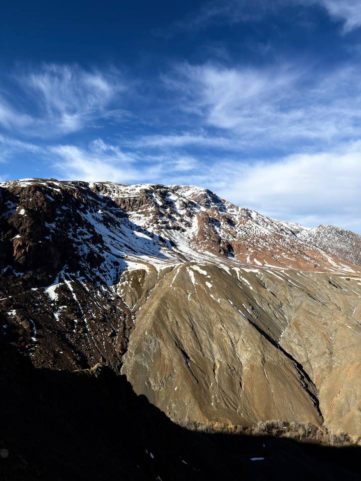 Snow-dusted ridges of the High Atlas Mountains rise against a bright blue sky.