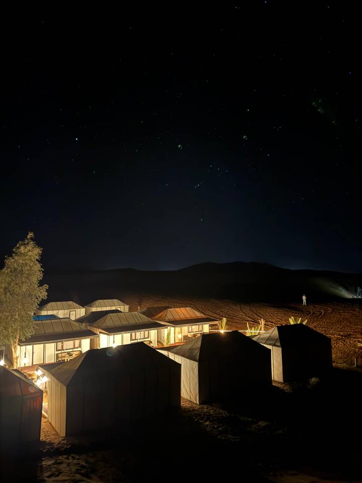 Luxury desert camp tents glow under a star-filled night sky, silent dunes surrounding the scene.