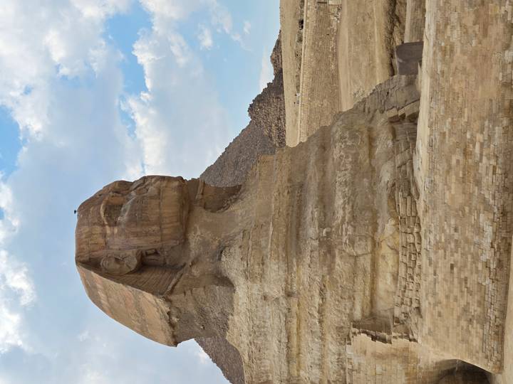 Close-up profile of the Great Sphinx with desert backdrop and partly cloudy blue sky.