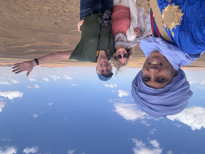 Travellers pose with their Berber guide overlooking Morocco’s vast desert landscape under blue skies.