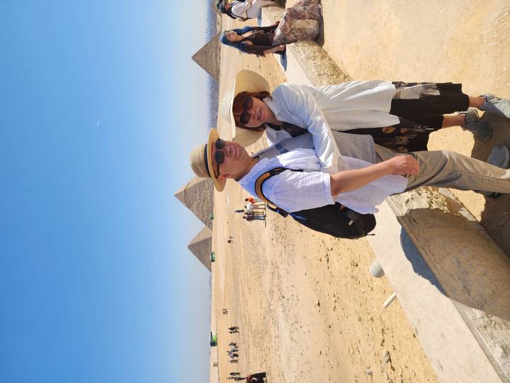 Couple embraces with the Great Pyramids of Giza rising behind them under a clear sky.