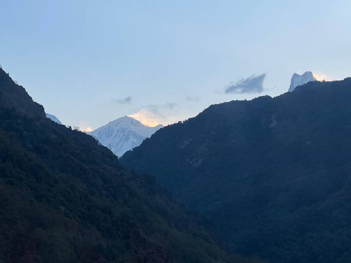 Distant snowy peaks peeking through dark green mountain ridges under a pale sky.