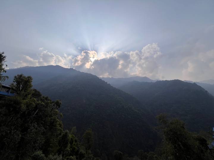 Sunbeams break through dramatic clouds above densely forested ridges in the Himalaya.