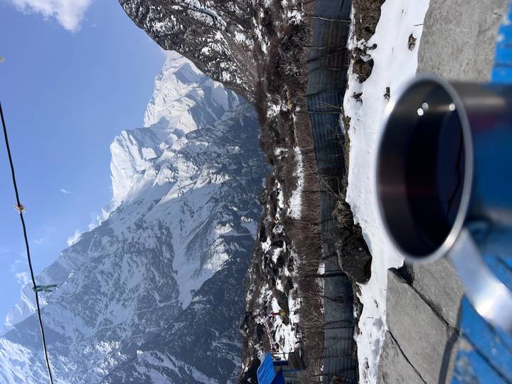 Steaming mug in the foreground with dramatic snowy peaks of the Annapurna Sanctuary beyond a wire fence.