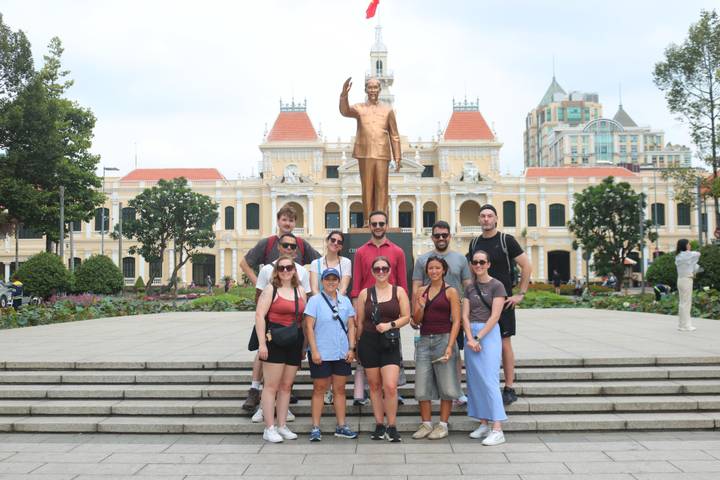 Tour group poses on the steps before the bronze Ho Chi Minh statue and French-colonial City Hall façade in Ho Chi Minh City.