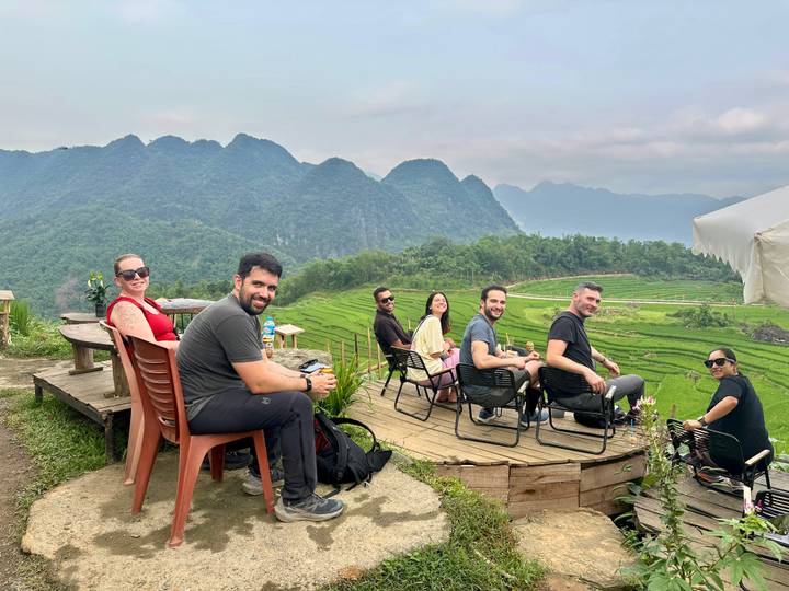 Travellers relax on a wooden deck overlooking emerald rice terraces and misty limestone peaks.