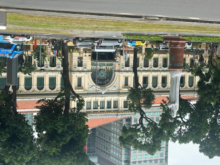 Historic Saigon Central Post Office with clock façade framed by tall trees and city traffic in the foreground.