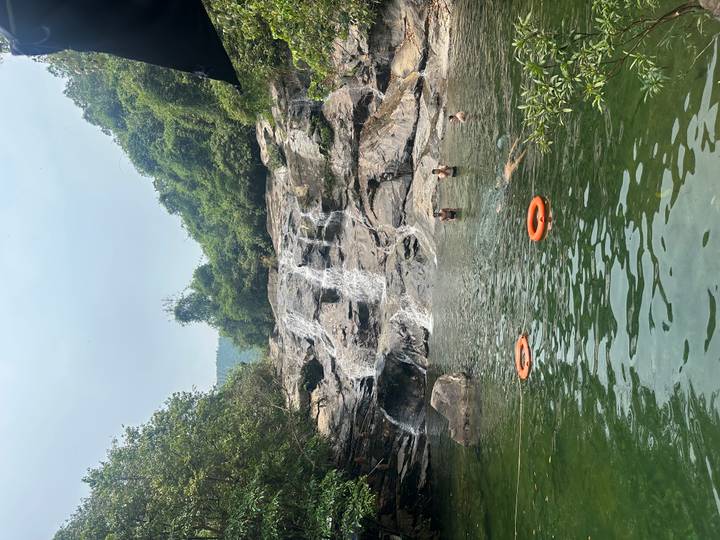 Travellers swim beneath a rocky jungle waterfall spilling into a clear natural pool.