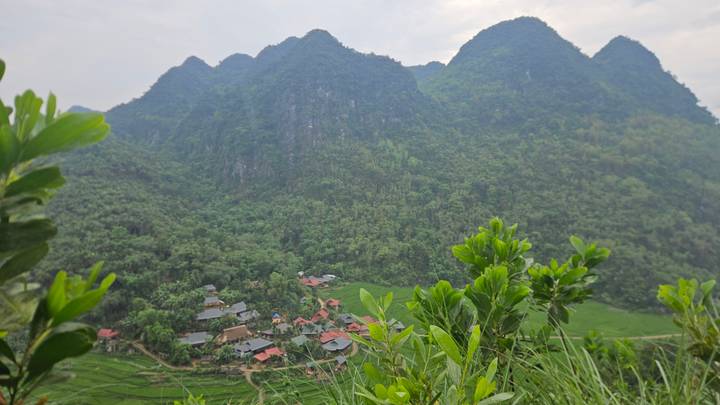 Green valley village with red-roof houses nestled below dramatic limestone karst mountains.