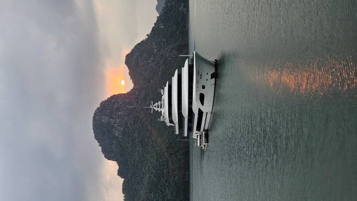 Luxury white cruise ship anchored in the emerald waters of Ha Long Bay at sunset with limestone karsts silhouetted behind.