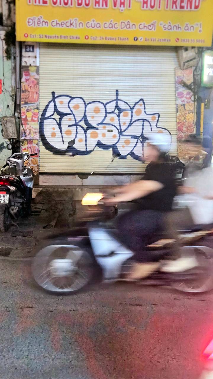 Motion-blurred motorbike rider speeds past graffiti-covered shutters on a city street at night.