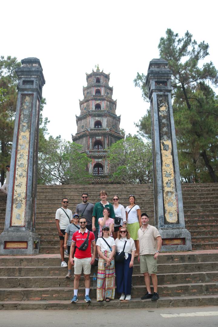 Tour group poses in front of the tall tiered Thien Mu Pagoda framed by ancient stone pillars.