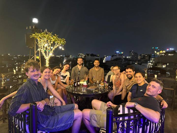 Group of travelers enjoy drinks at a rooftop bar overlooking city lights at night.