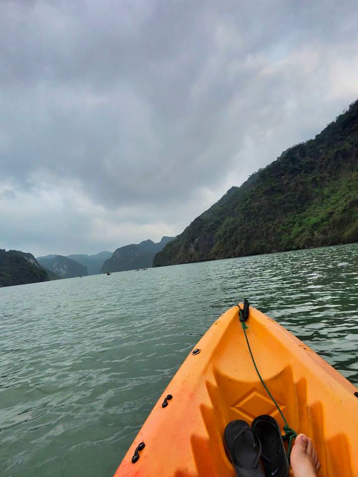 View from the bow of a kayak gliding through misty limestone peaks in Halong Bay.