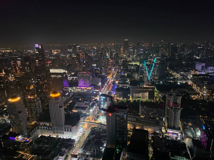Dramatic night skyline of Bangkok with countless illuminated skyscrapers and busy avenues seen from a rooftop.