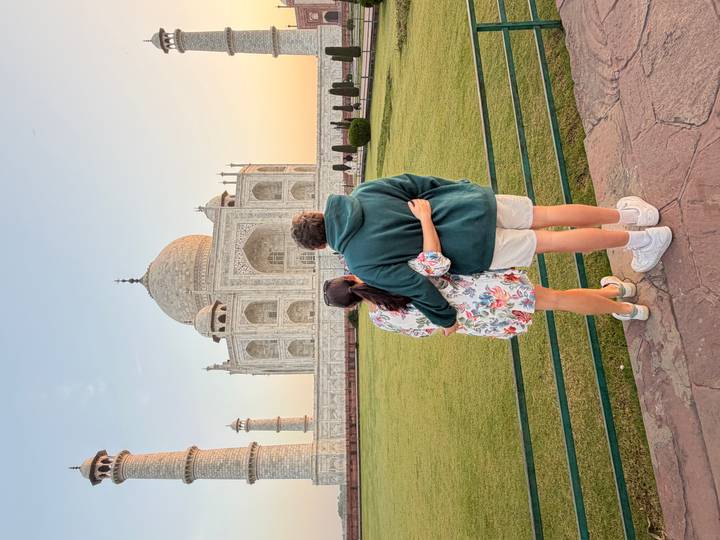 Couple embraces while admiring the Taj Mahal at sunset, standing on manicured lawns.