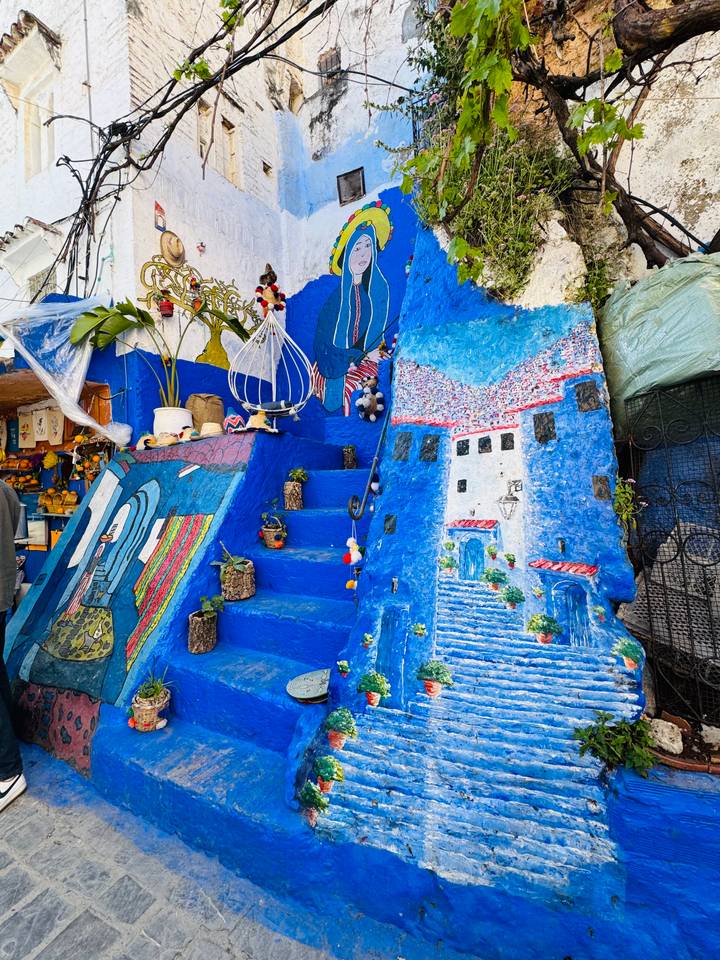 Vibrant blue staircase decorated with plants, paintings and crafts in the medina of Chefchaouen