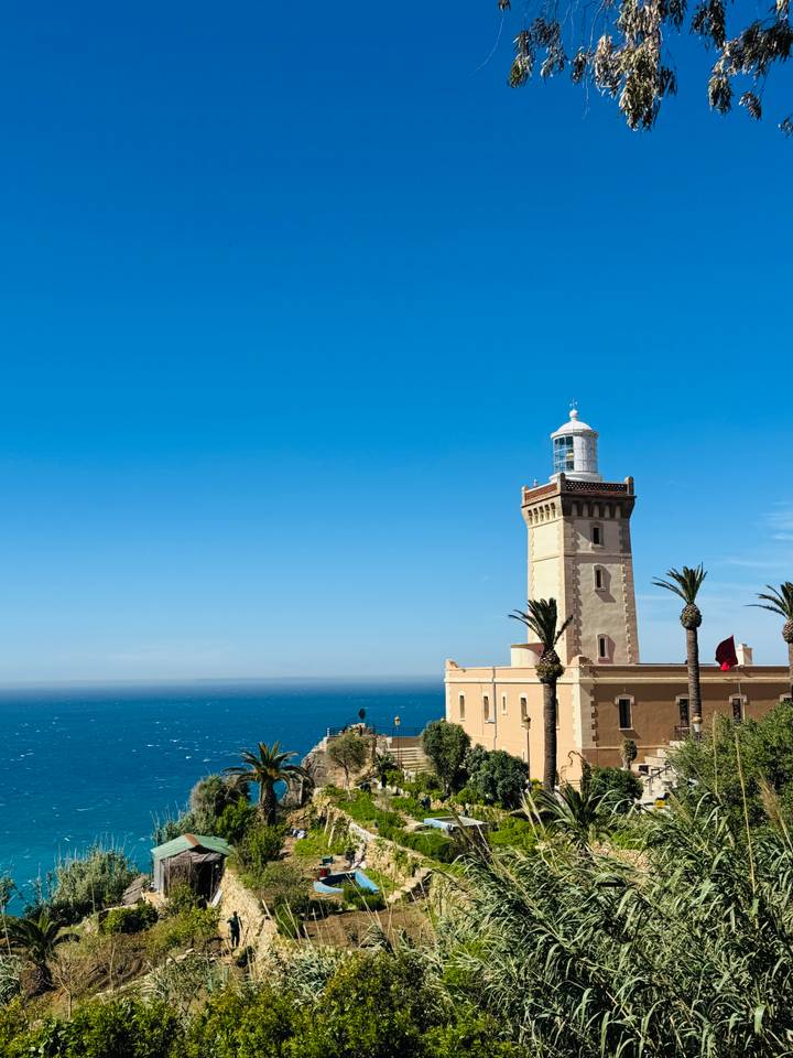 Cream-colored lighthouse with palm trees overlooks the Atlantic Ocean under a clear blue sky