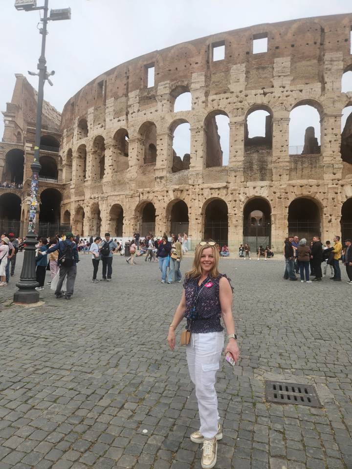 Tourists milling around the Colosseum while a woman smiles in the foreground wearing a tour badge