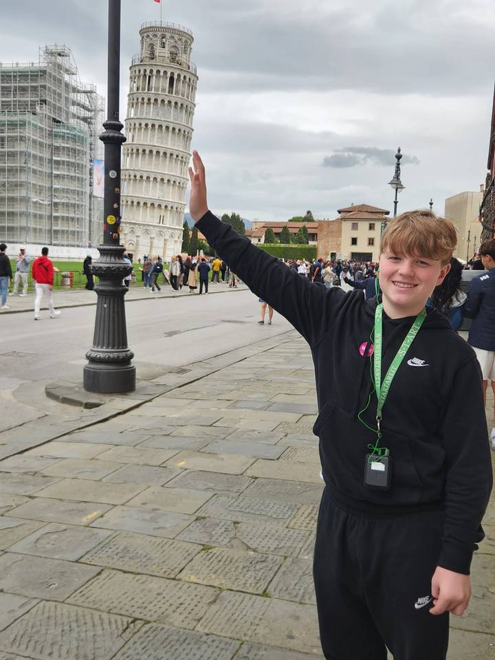 Teenager playfully posing as if holding up the Leaning Tower of Pisa among crowds on the piazza