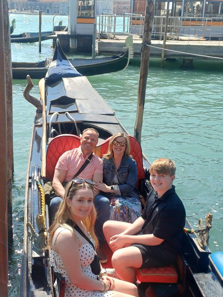 Family seated in a gondola on emerald waters of Venice’s canal with sunlight glinting