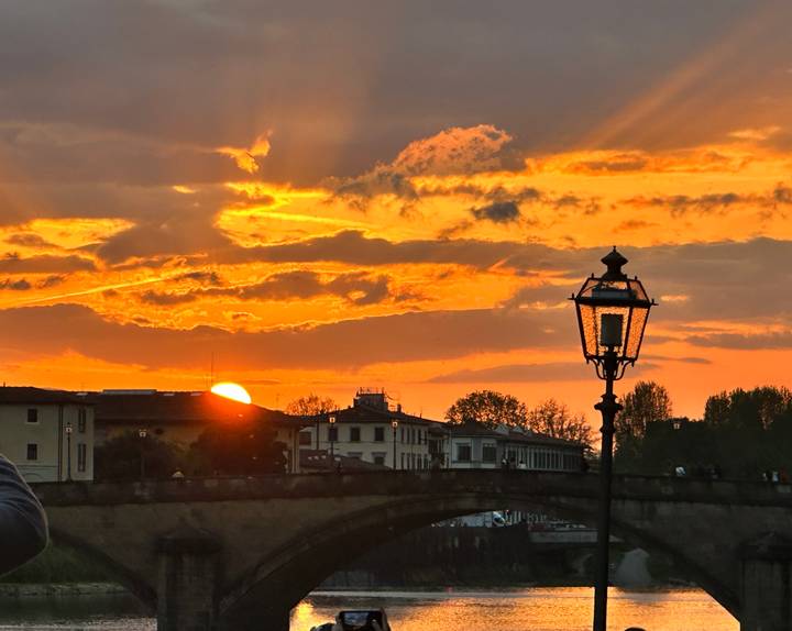 Setting sun over the Arno river with an antique street lamp silhouetted against an orange sky
