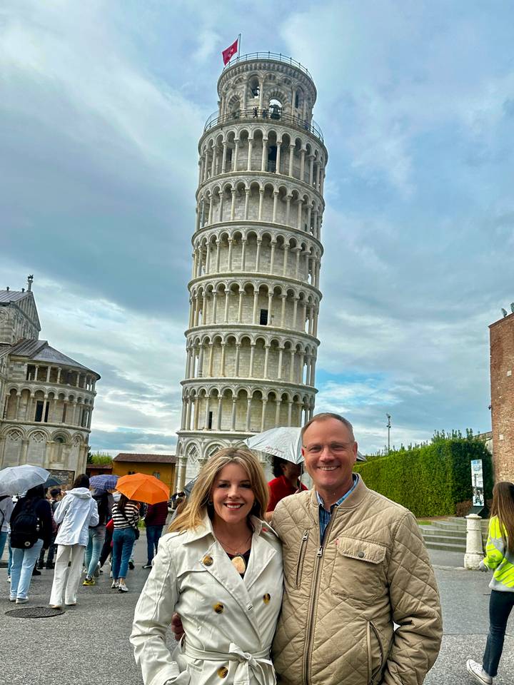 Couple posing with umbrellas in front of the Leaning Tower of Pisa on a cloudy day