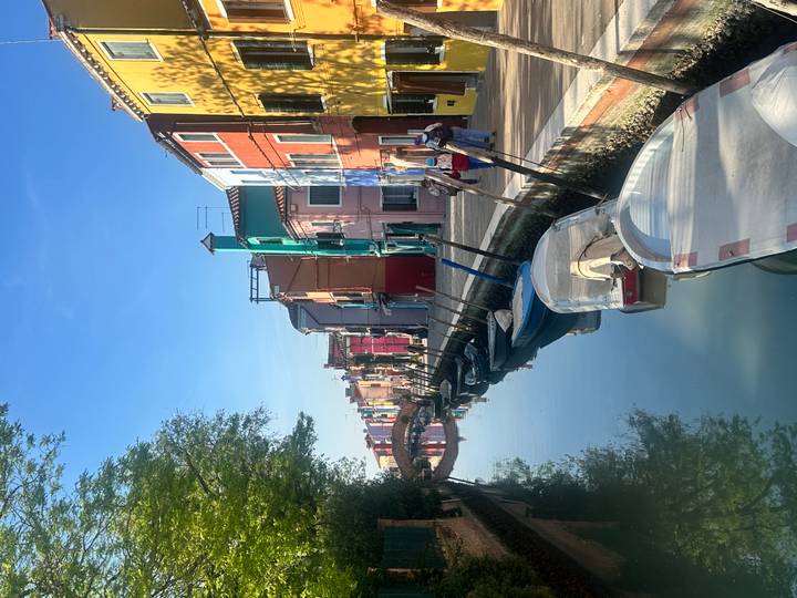 Colorful houses lining a calm canal in Burano with moored boats reflecting in the water