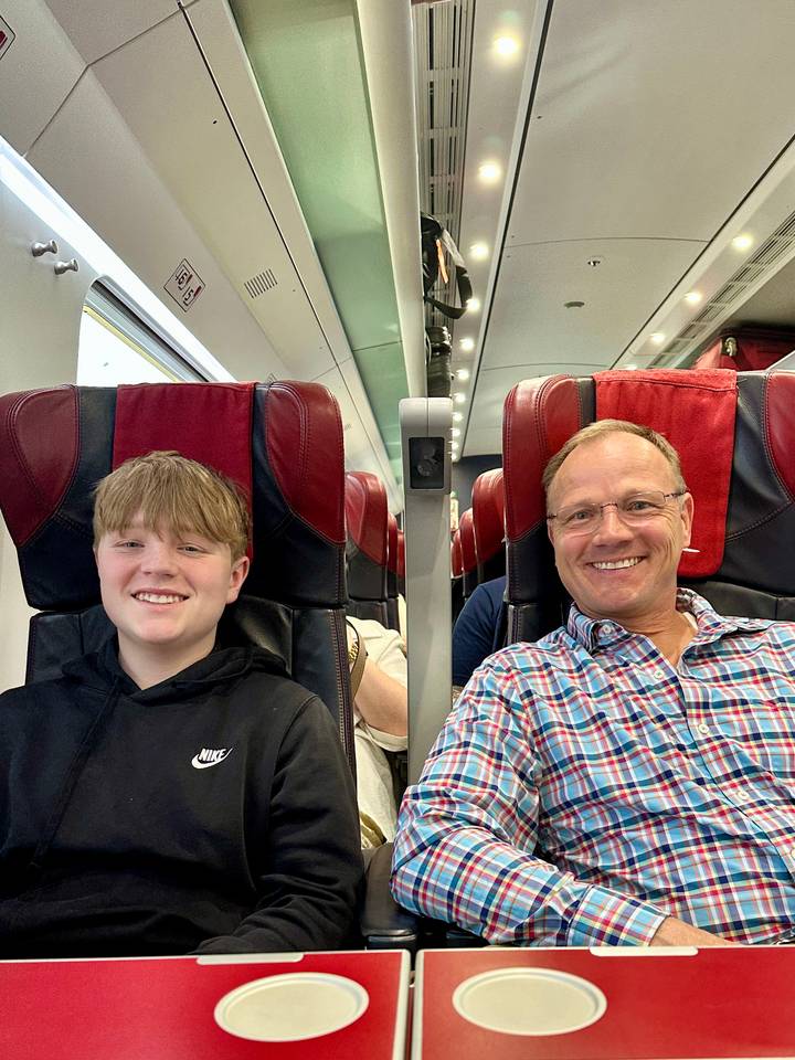 Father and son smiling while seated on red-trimmed seats inside a modern train carriage