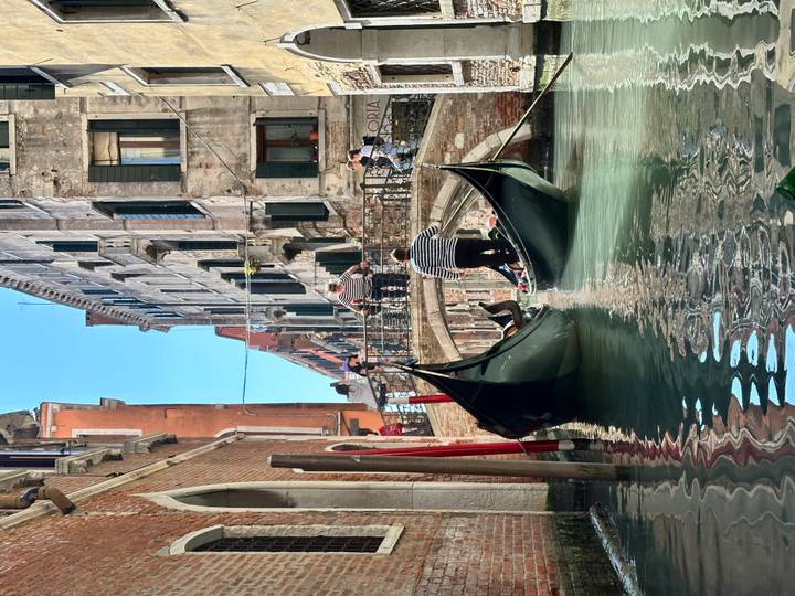 Two gondolas gliding beneath a stone footbridge between historic Venetian buildings on a clear day