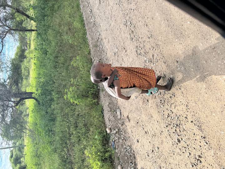 Young Maasai child carrying a smaller sibling on a rural dirt road.